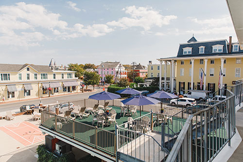 Outdoor seating with umbrellas on the sundeck and shuffleboard on the ground level. Congress Hall is visible in the background